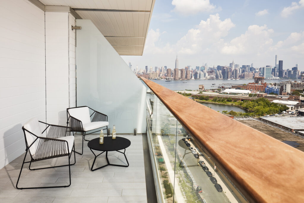 Modern balcony with two chairs, small table, and skyline view of Manhattan across the river.