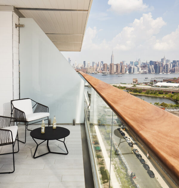 Modern balcony with two chairs, small table, and skyline view of Manhattan across the river.