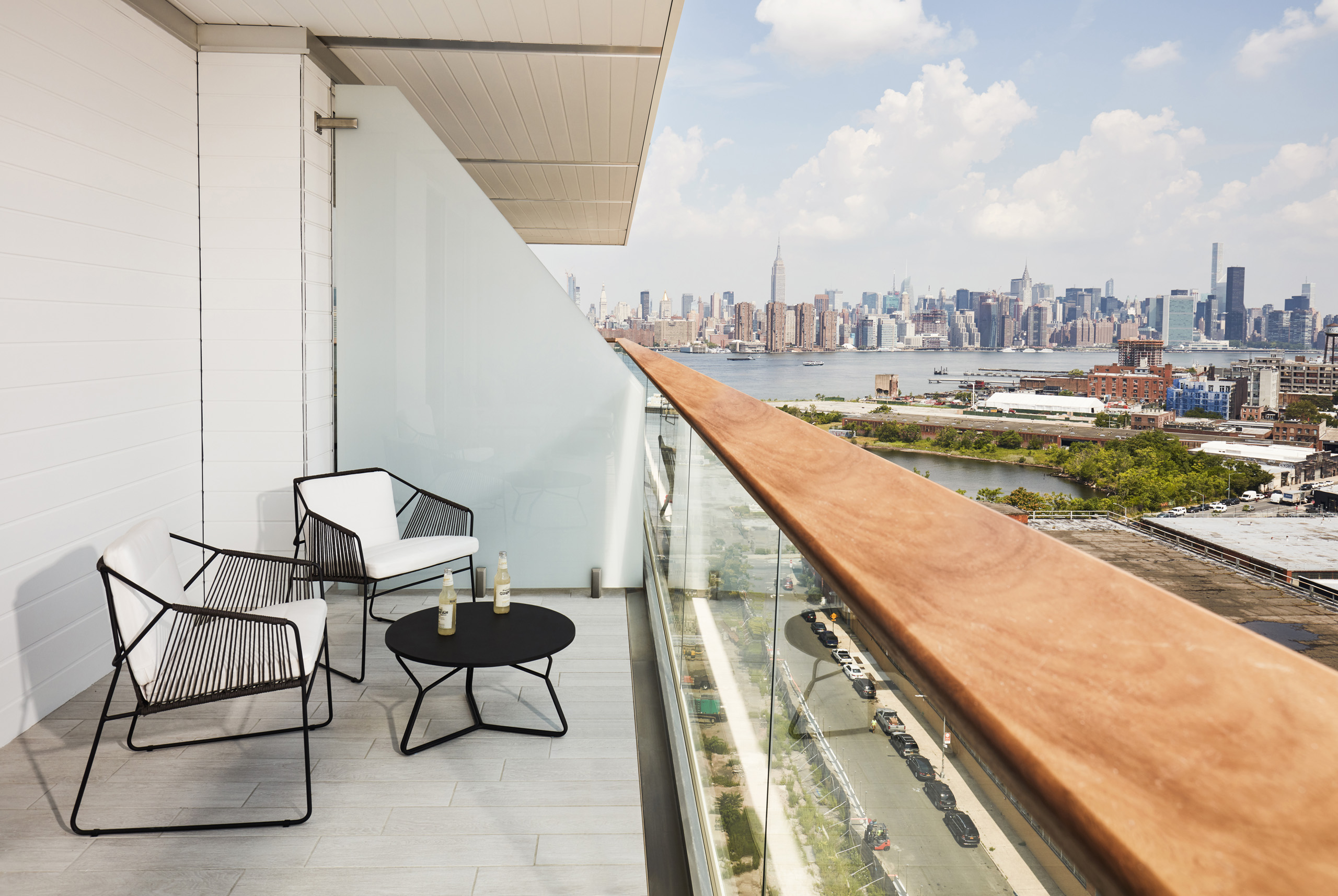 Modern balcony with two chairs, small table, and skyline view of Manhattan across the river.