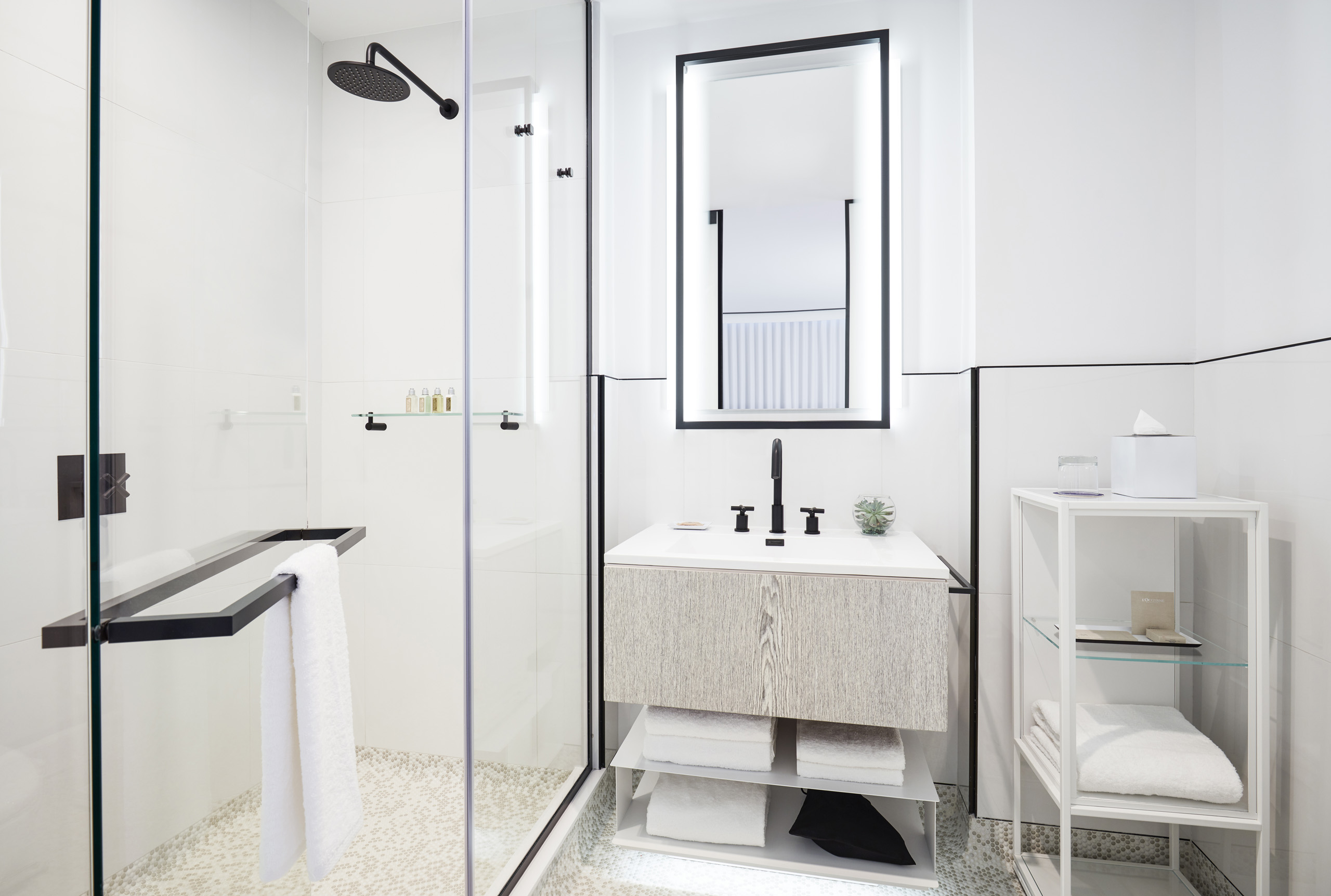 Sleek bathroom with walk-in shower, illuminated mirror, and black fixtures.