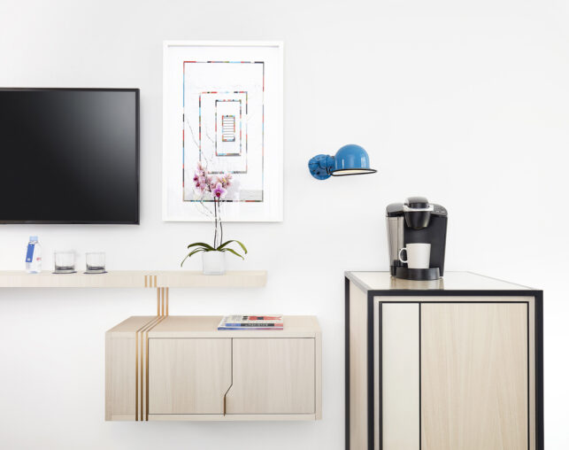 Wall-mounted TV and coffee station with orchid and artwork.