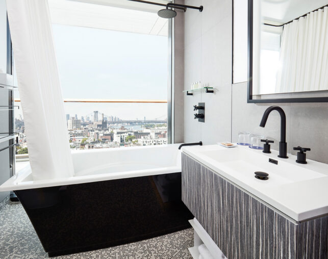Modern bathroom with tub and city skyline view.