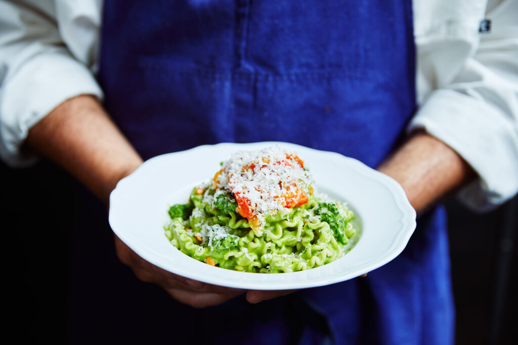 Chef holding pasta topped with vegetables and grated cheese.