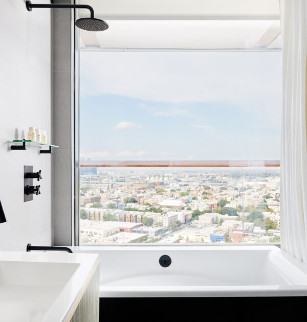 Modern bathroom with black fixtures, deep soaking tub, and city view through large window.