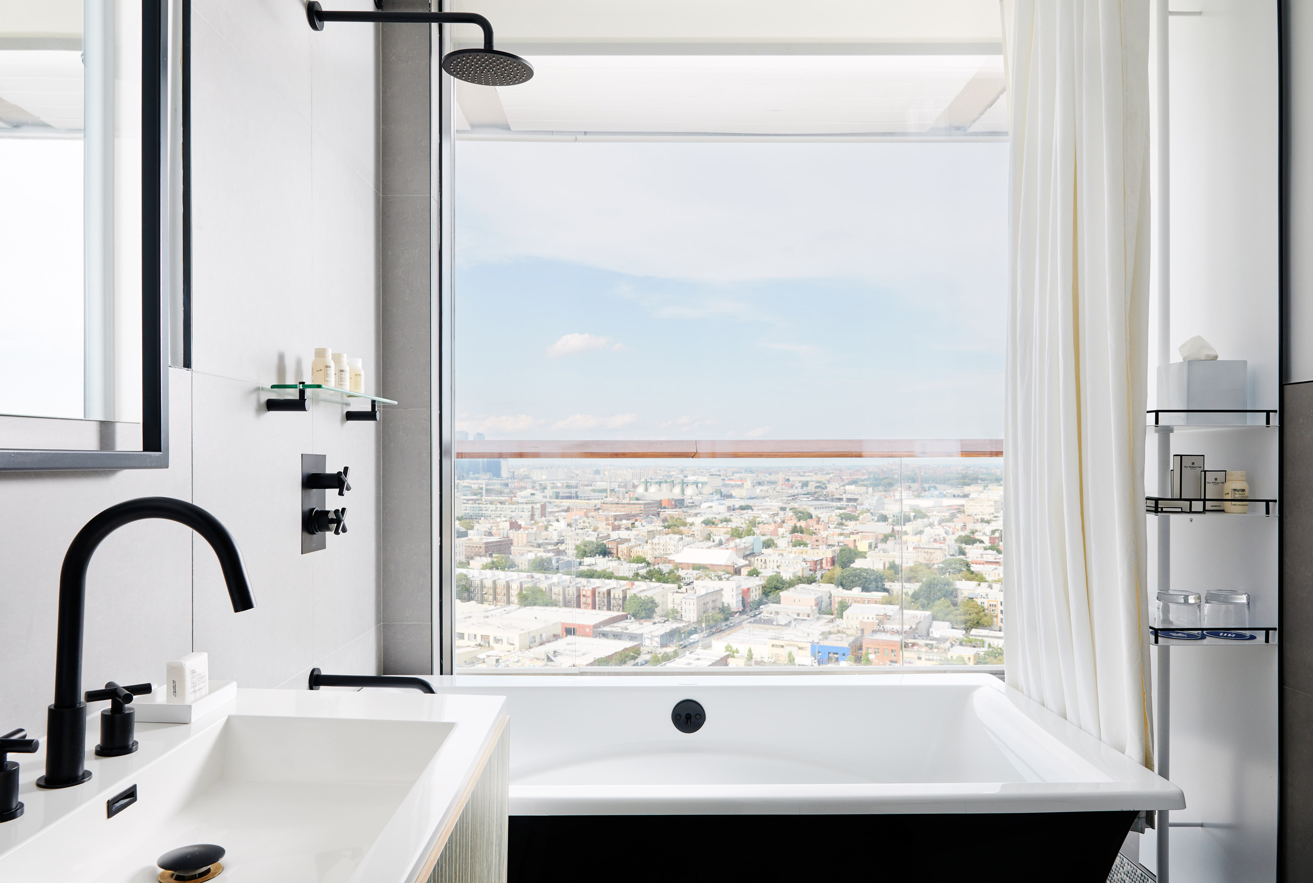 Modern bathroom with black fixtures, deep soaking tub, and city view through large window.