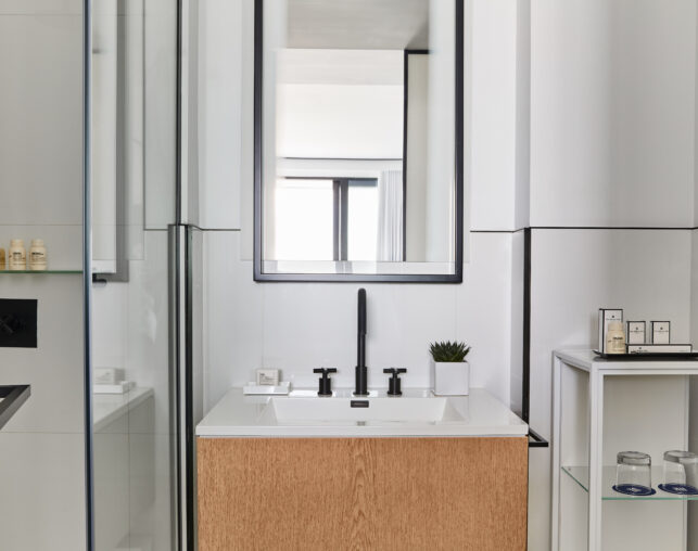 Contemporary bathroom vanity with black fixtures and shower reflection.