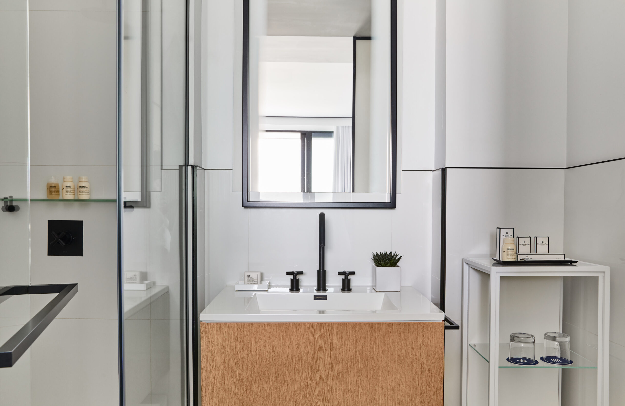 Contemporary bathroom vanity with black fixtures and shower reflection.