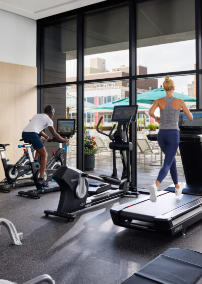 People exercising on treadmills, bikes, and weight benches indoors.