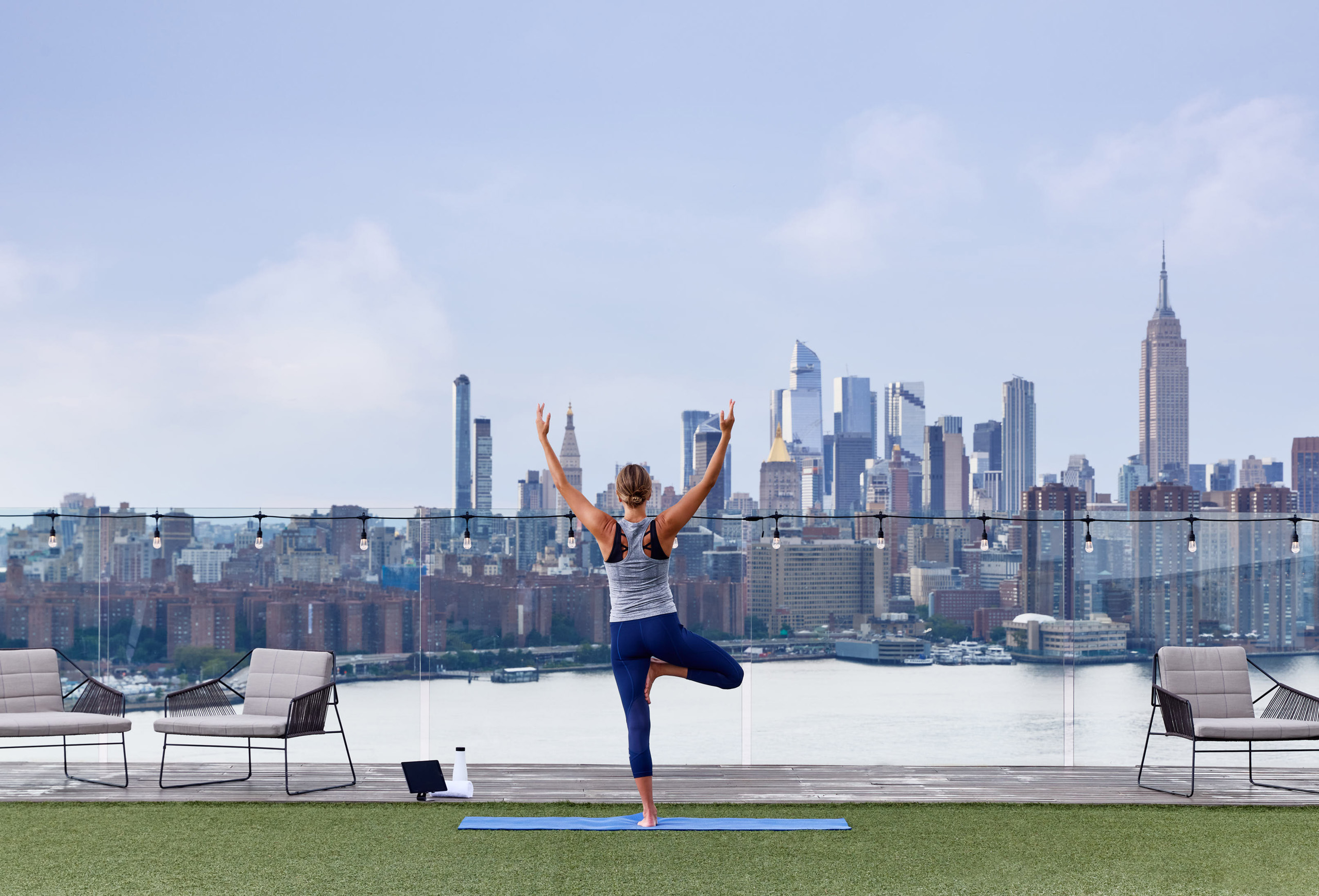 Person practicing yoga on a rooftop with Manhattan skyline backdrop.
