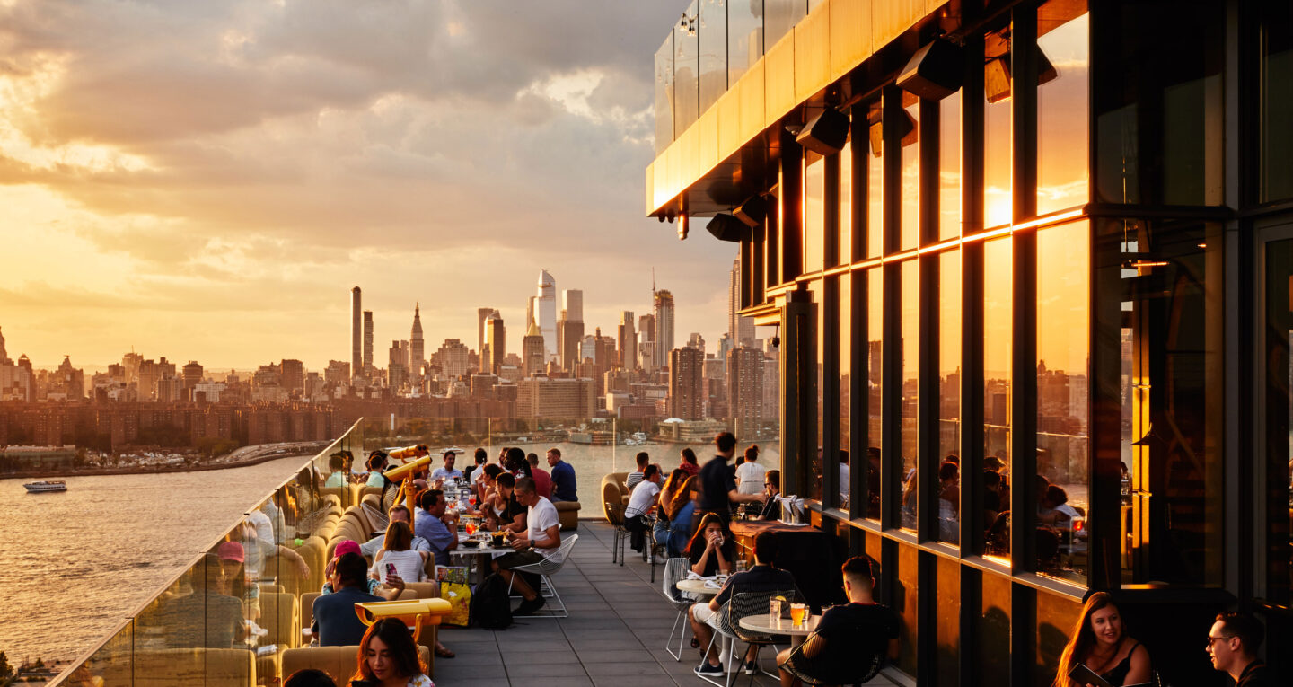 Rooftop restaurant with people dining at sunset skyline view.