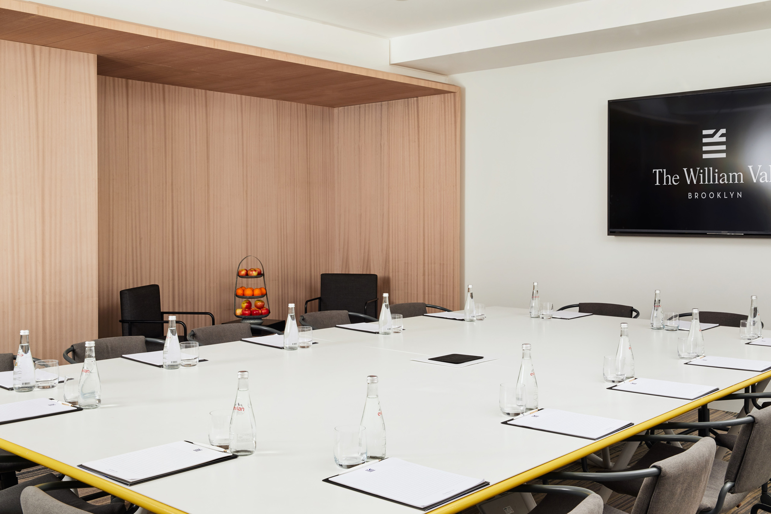 Boardroom with The William Vale screen, white notepads, and a tiered fruit display.