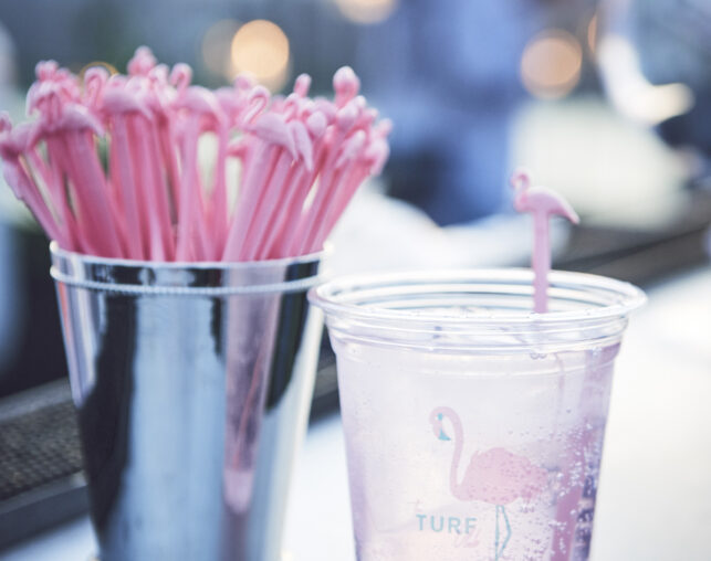 Clear cup with pink drink stirrer and flamingo design next to a bucket of stirrers.
