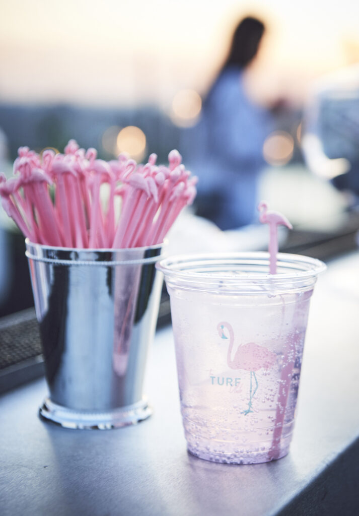 Clear cup with pink drink stirrer and flamingo design next to a bucket of stirrers.