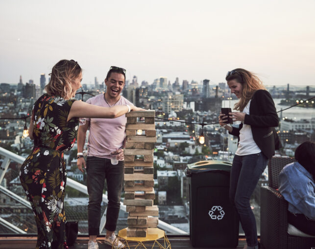 Friends laughing while playing giant Jenga on a rooftop.
