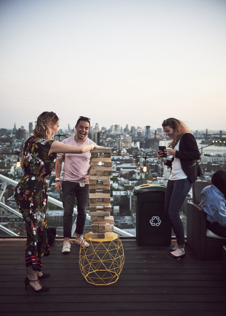 Friends laughing while playing giant Jenga on a rooftop.