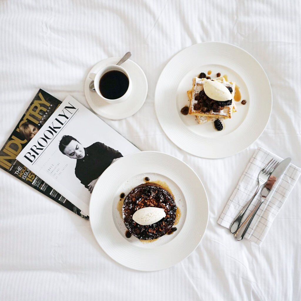 Breakfast plates with coffee and magazine on bed.