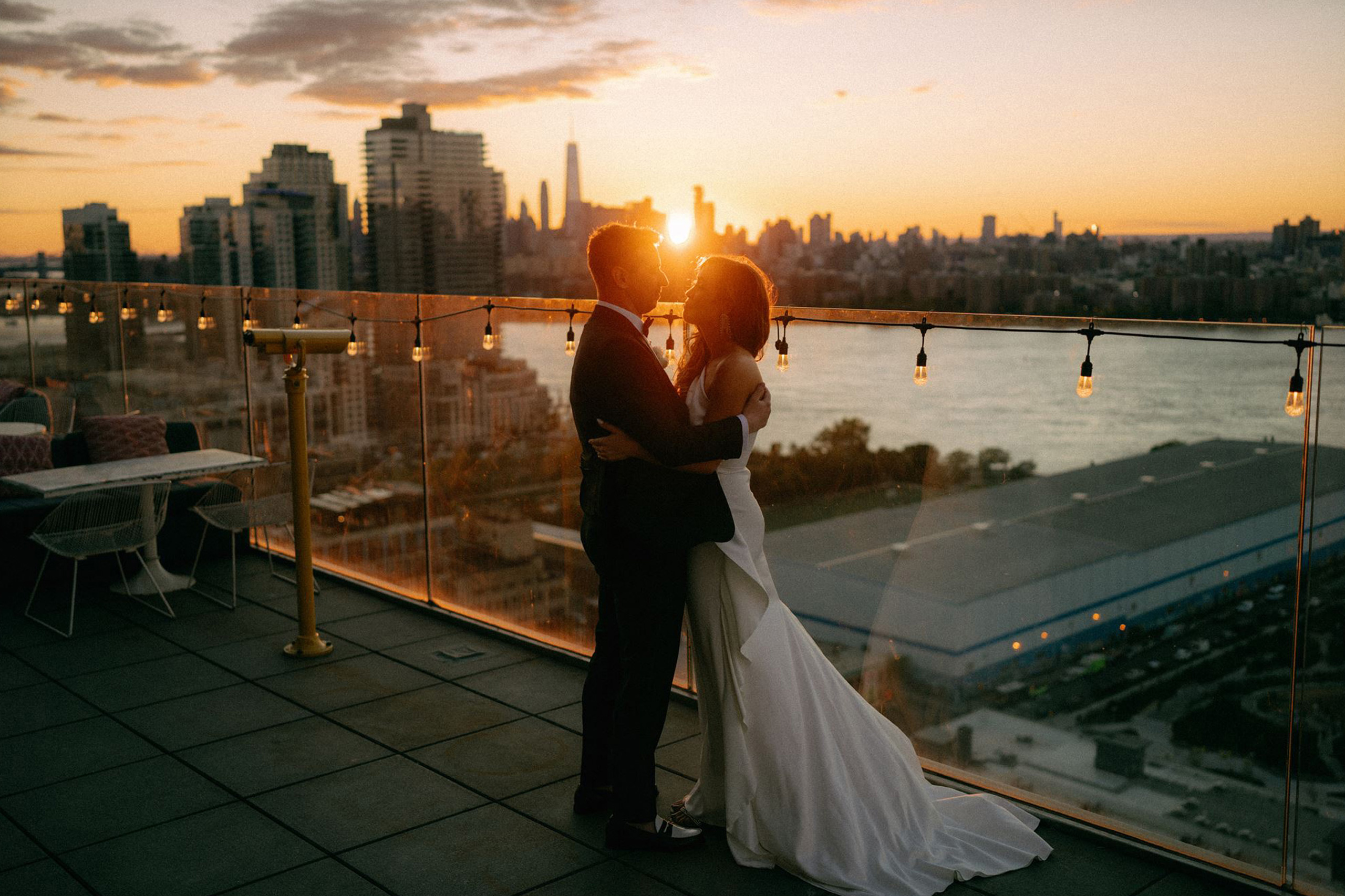 Bride and Groom embracing on a rooftop at sunset with city lights behind them.