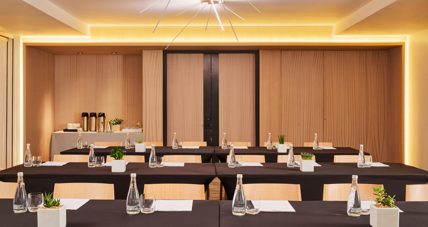 Modern meeting space with black tablecloths, plants, and water bottles.