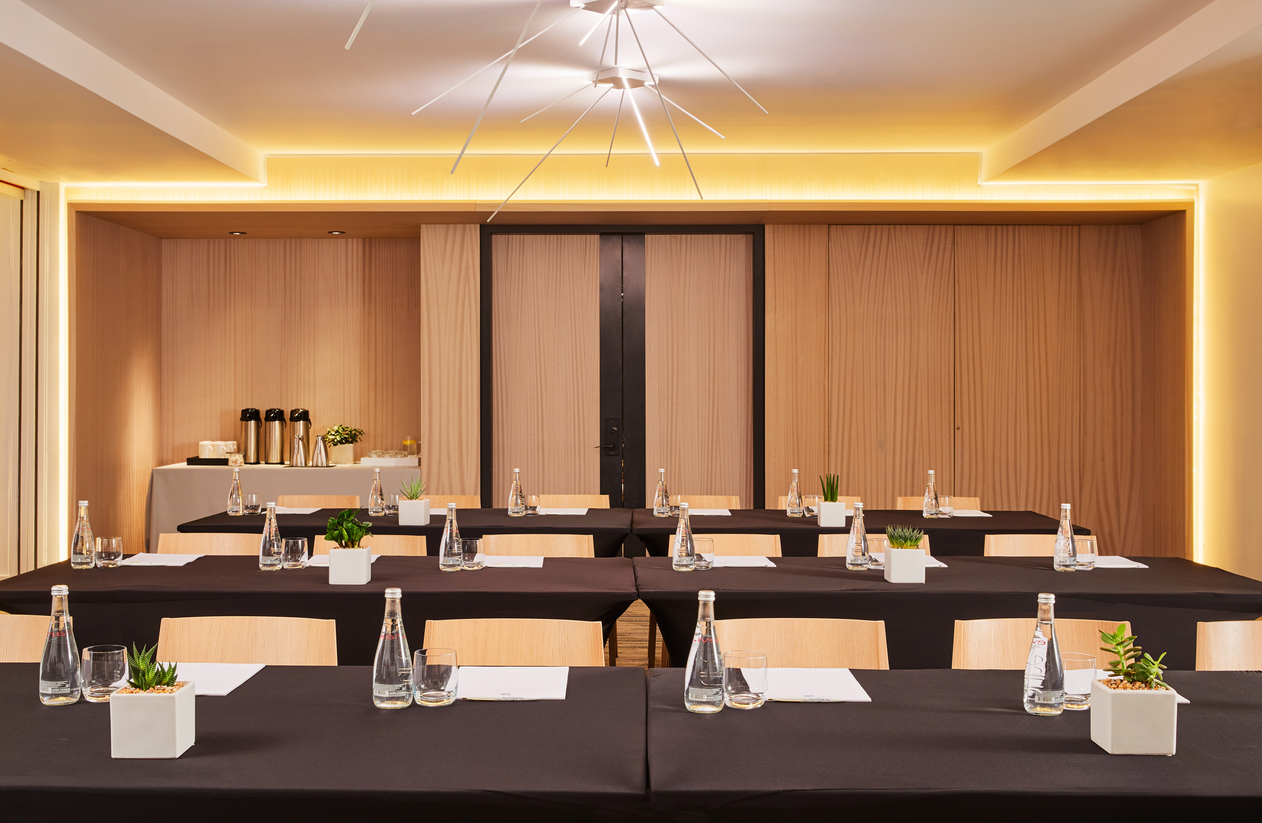 Modern meeting space with black tablecloths, plants, and water bottles.