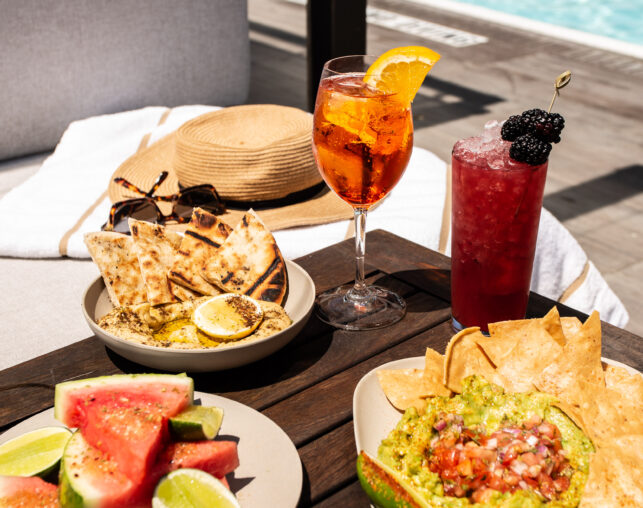 Poolside table with cocktails, watermelon, guacamole, and pita bread.
