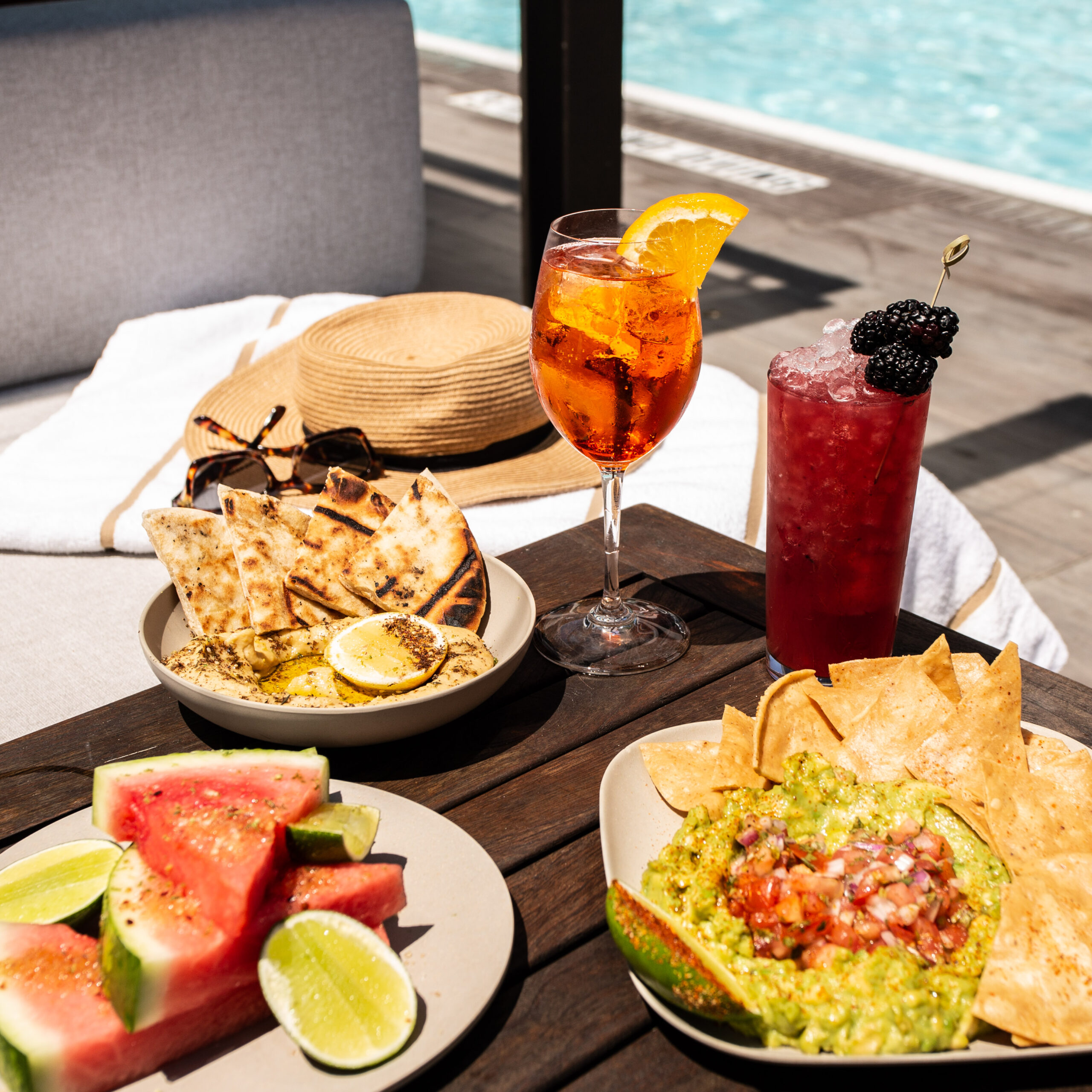 Poolside table with cocktails, watermelon, guacamole, and pita bread.