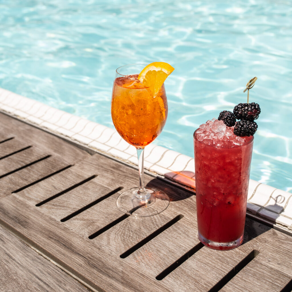 Two cocktails beside a rooftop pool.