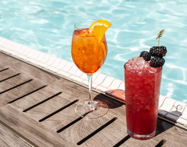 Two cocktails beside a rooftop pool.