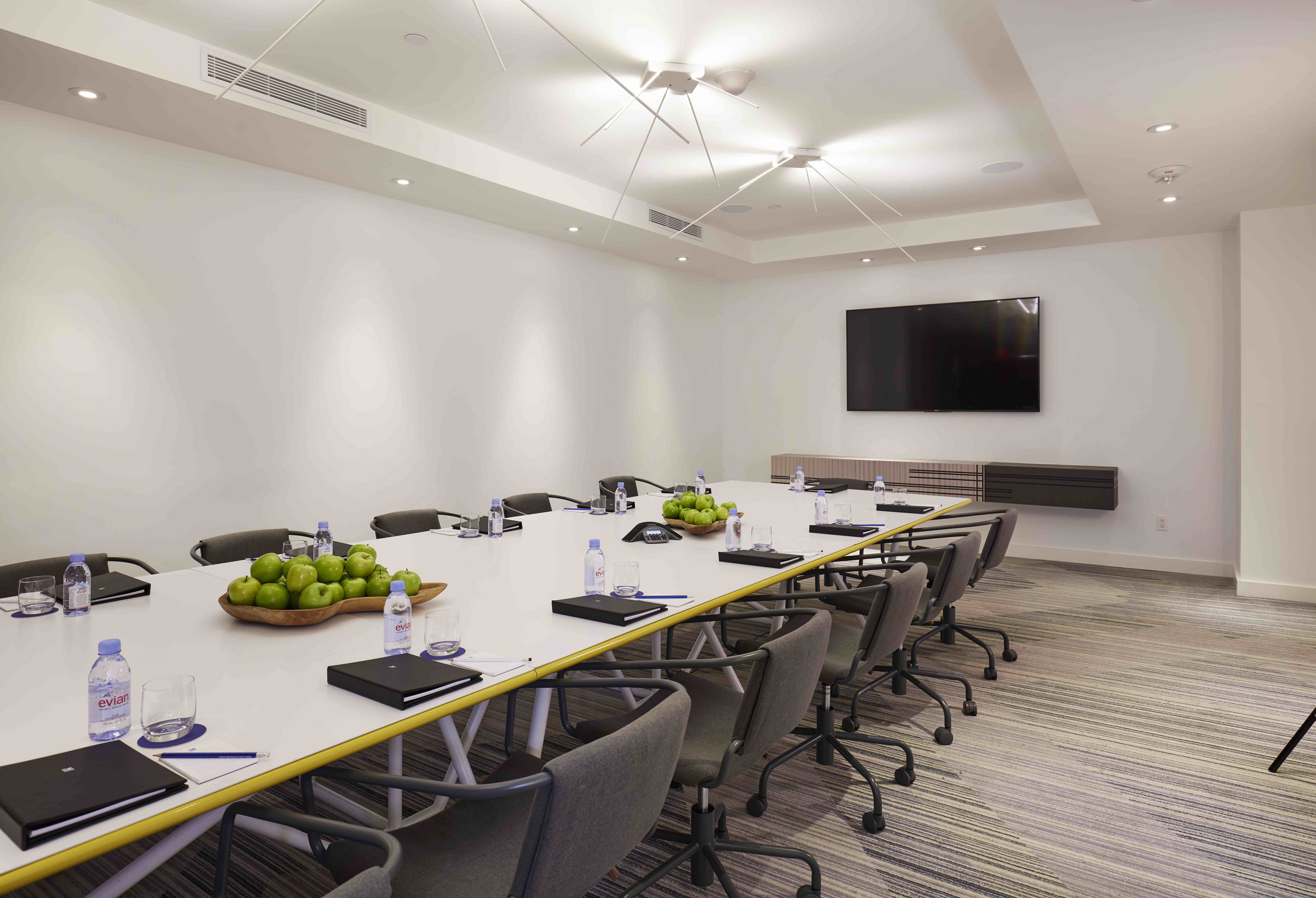 Modern boardroom with long table, rolling chairs, and green apples as centerpieces.