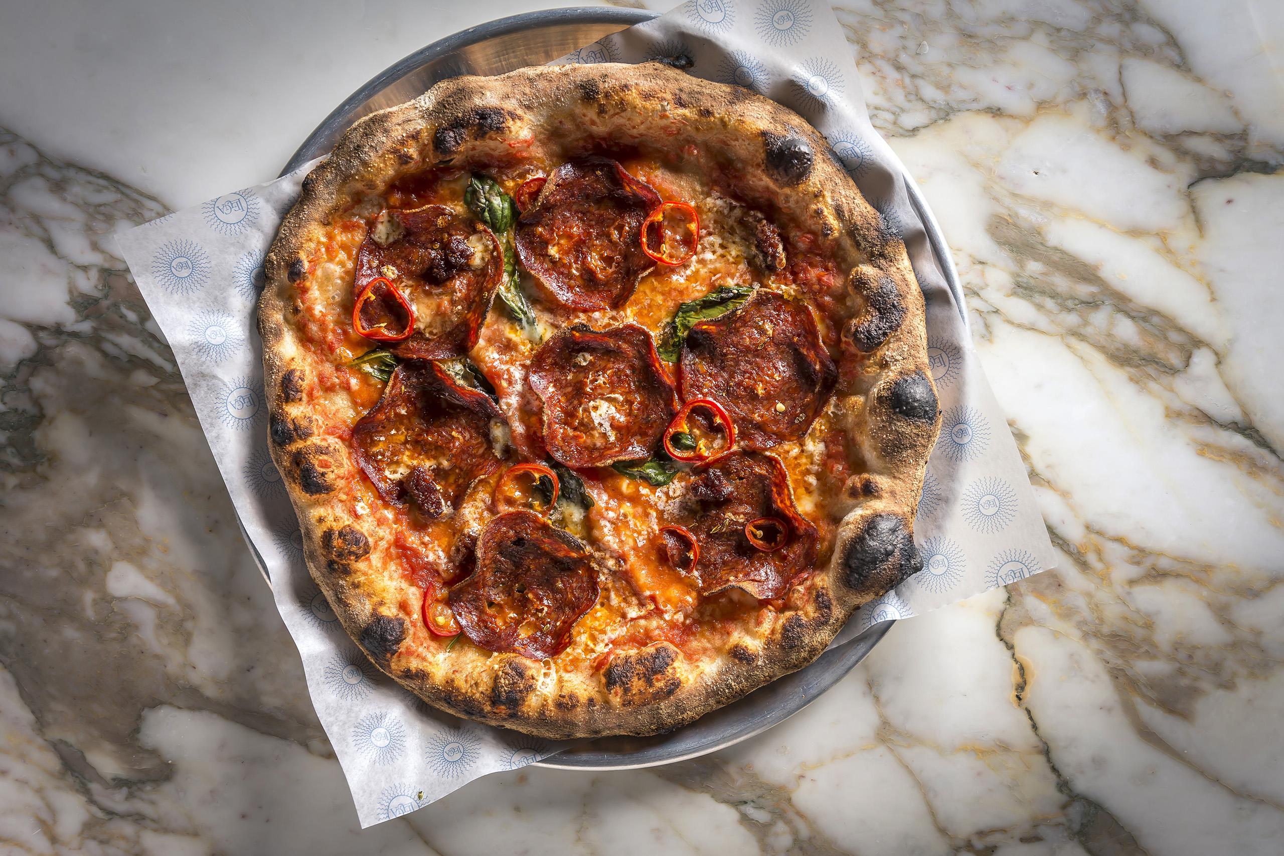 Wood-fired pepperoni pizza with basil and chili slices.