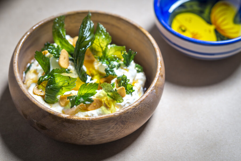 Wooden bowl of creamy dip topped with herbs.