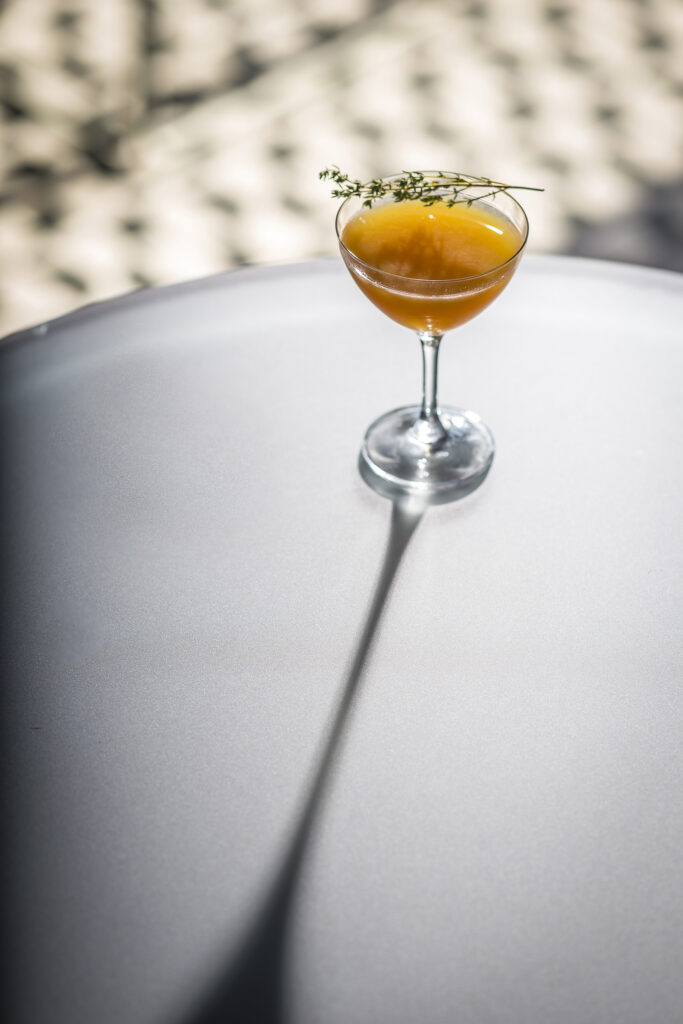 Orange cocktail in a coupe glass casting a long shadow.