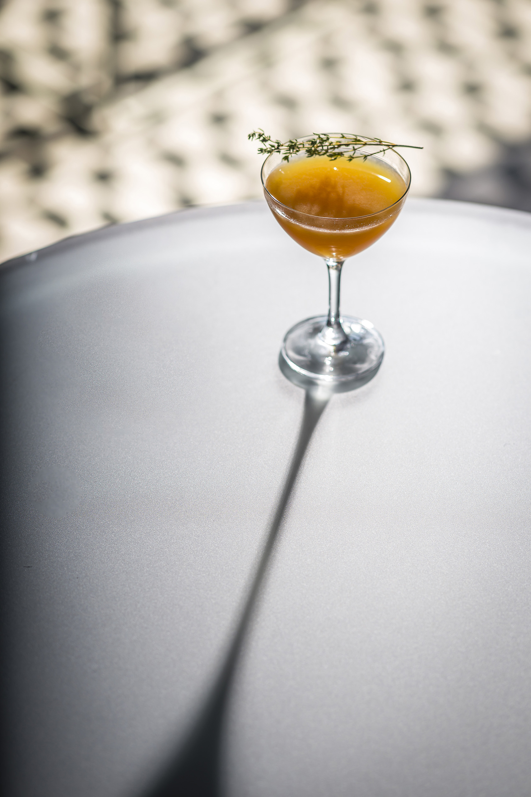 Orange cocktail in a coupe glass casting a long shadow.