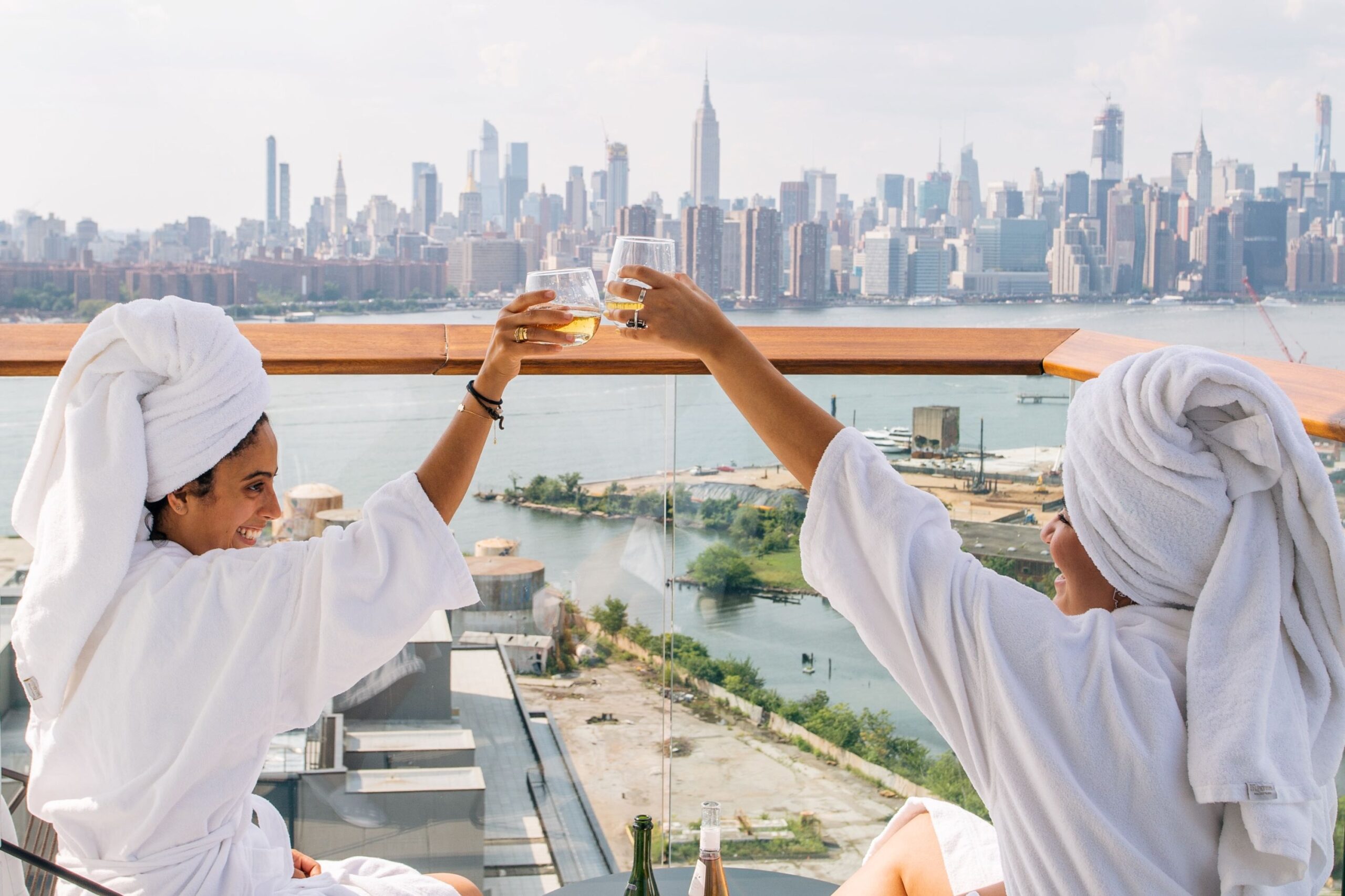 Two guests clink champagne glasses from their private balcony with the Manhattan skyline in the distance.