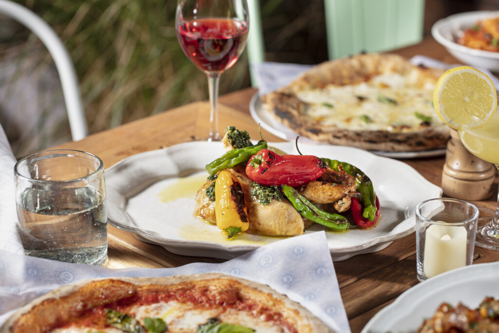 Colorful roasted chicken with peppers and wine on table.