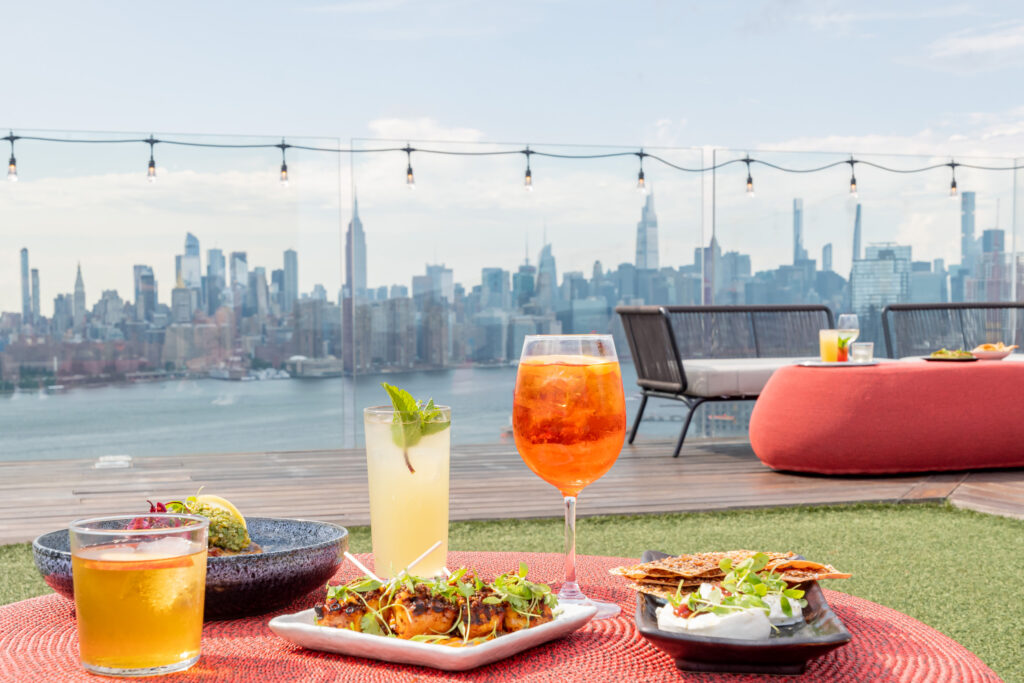 Colorful cocktails and small plates with city skyline view from rooftop.