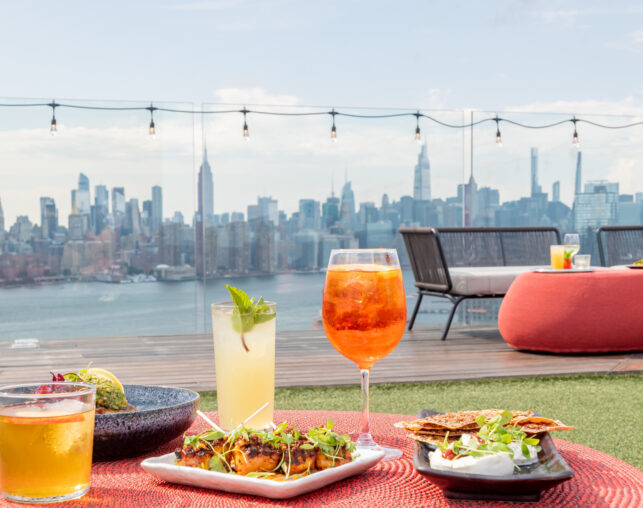 Colorful cocktails and small plates with city skyline view from rooftop.