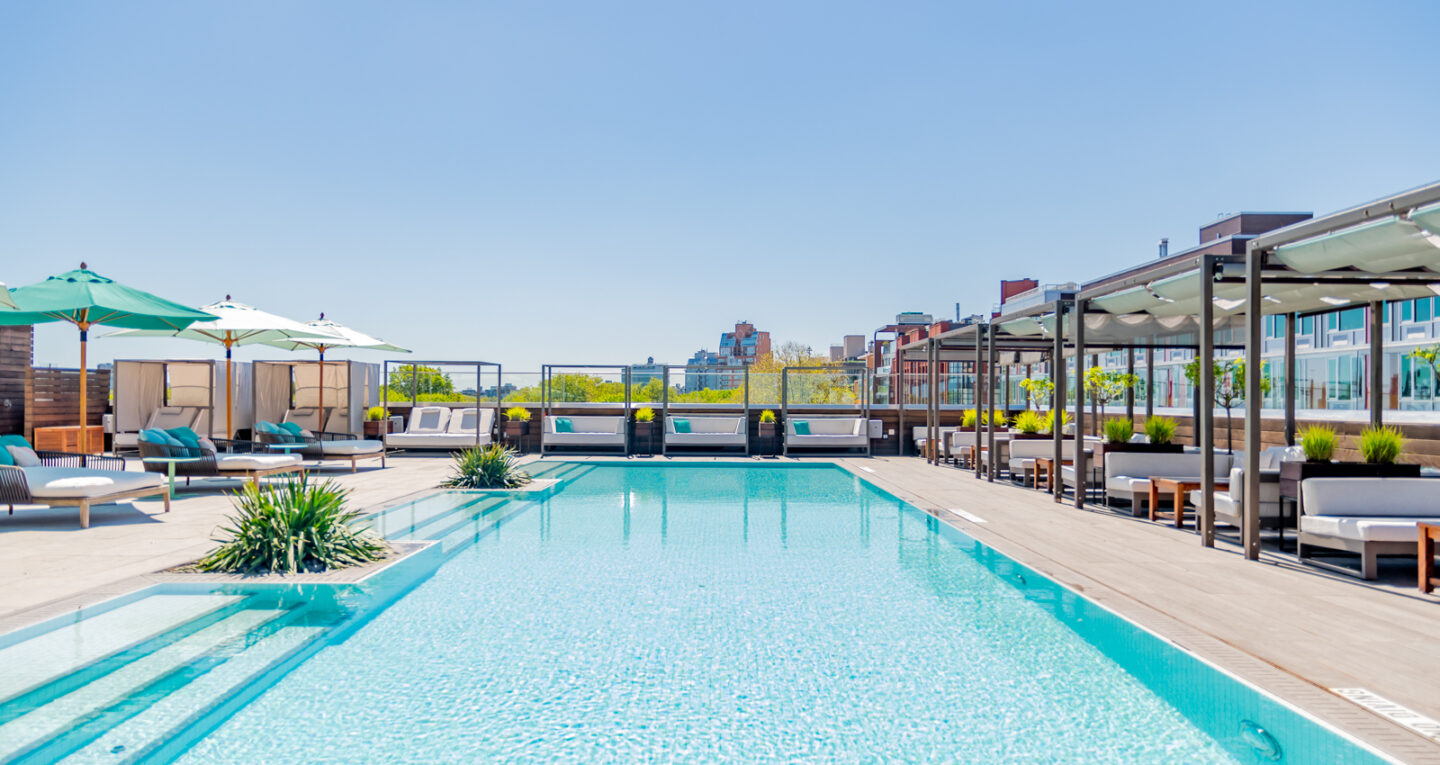 Rooftop pool with cabanas, lounge chairs, and umbrellas.