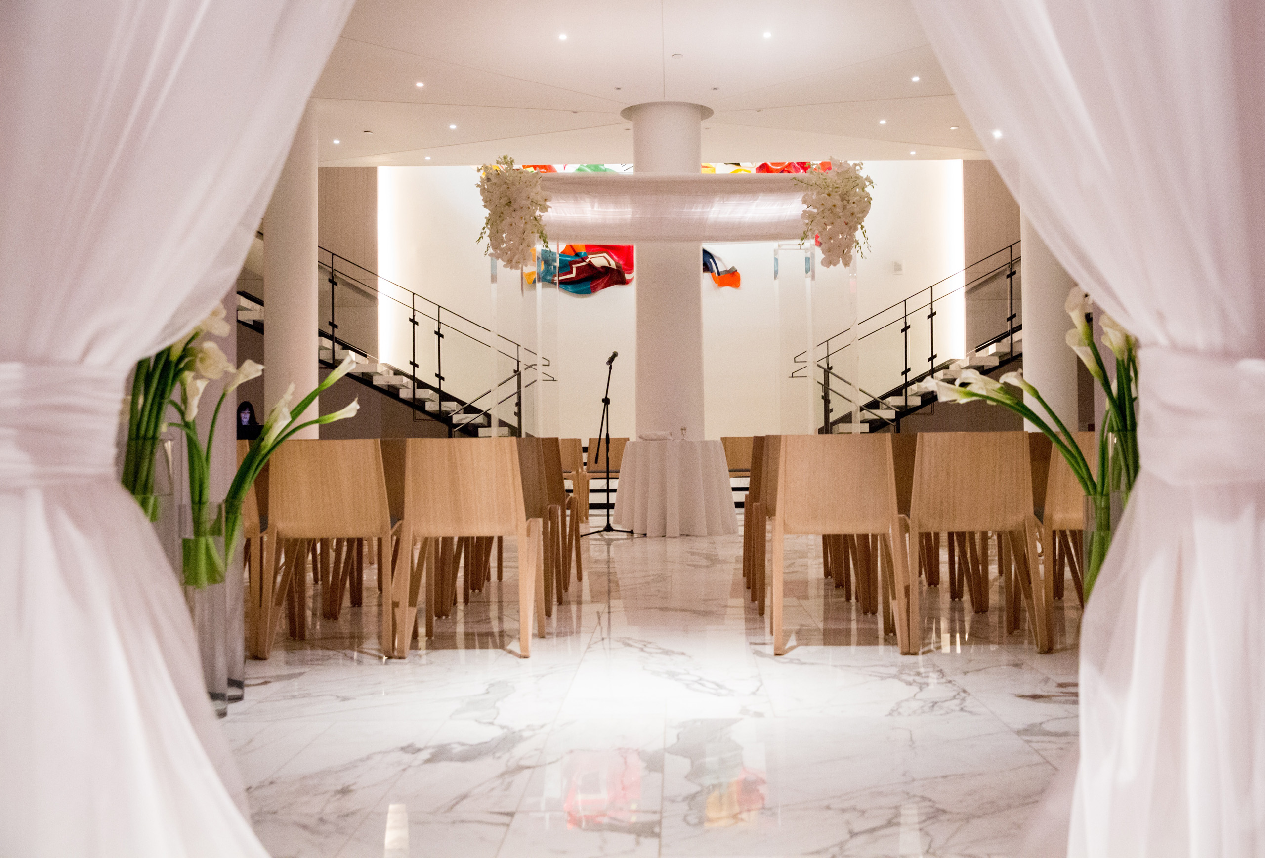 Elegant ceremony setup with wooden chairs and floral arch between twin staircases.