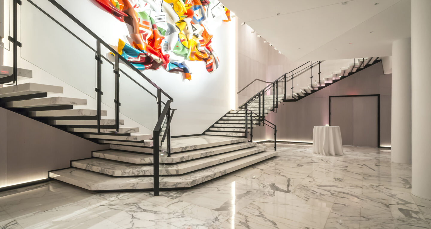 Modern marble staircase with glass railing and colorful abstract wall sculpture.