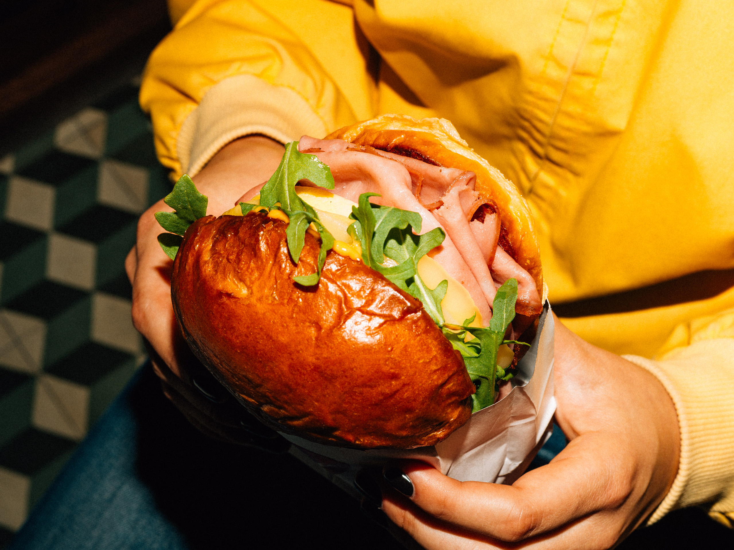 Hands holding sandwich with ham and arugula
