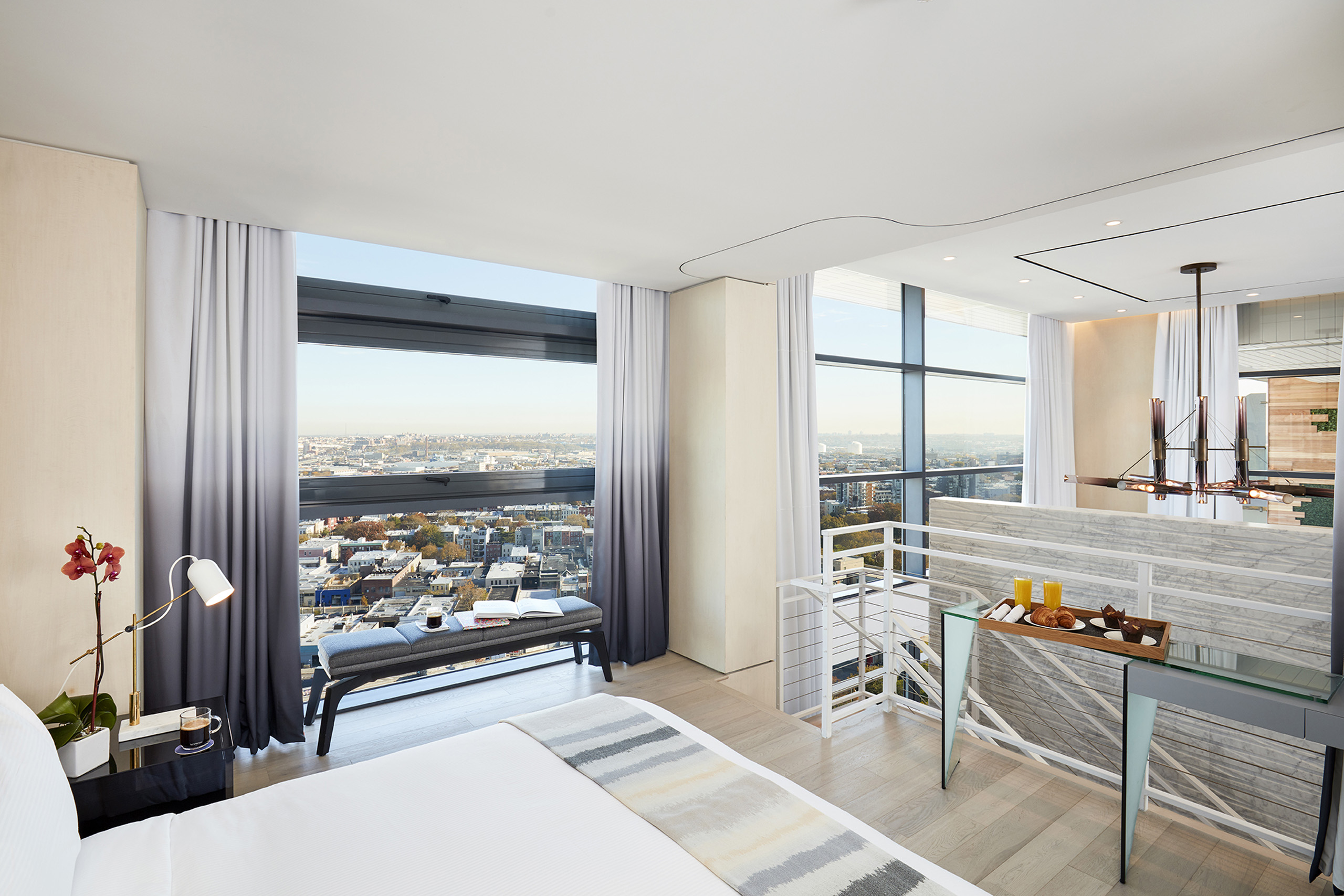 Loft bedroom with large windows and expansive city views.