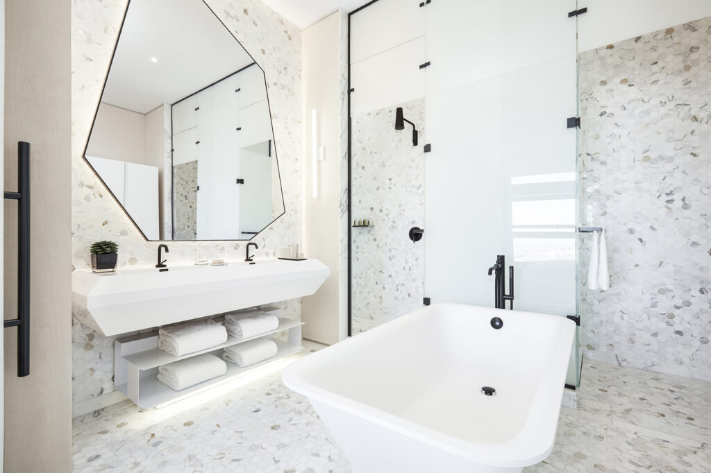 Bright bathroom with tub, double sink, and geometric mirror.