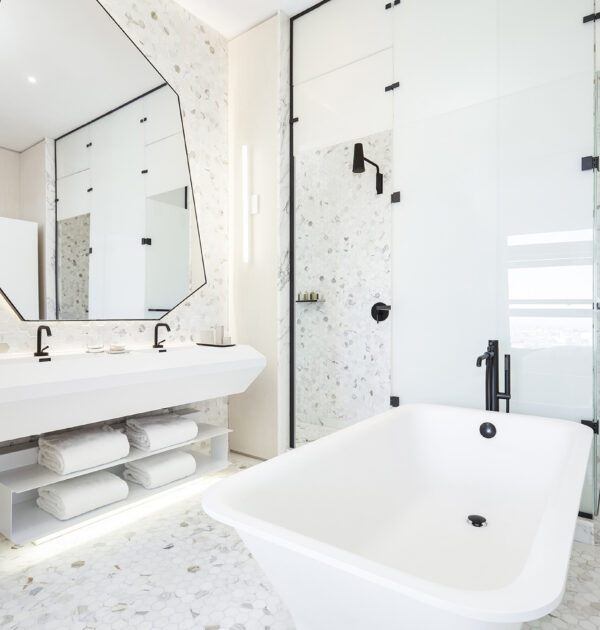 Bright bathroom with tub, double sink, and geometric mirror.