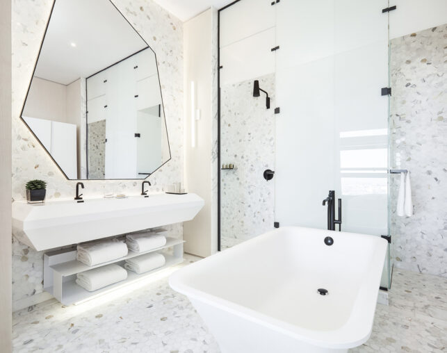 Bright bathroom with tub, double sink, and geometric mirror.