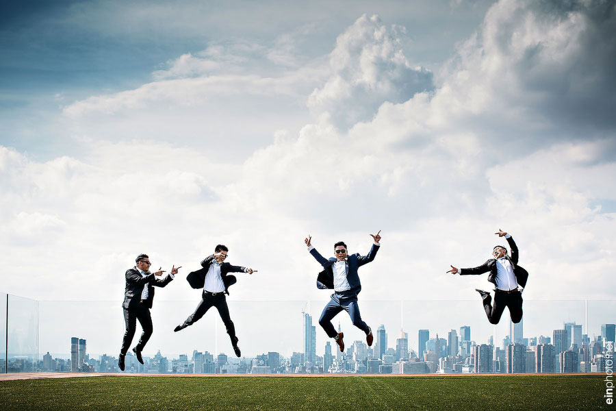 Four groomsmen jumping on rooftop with city backdrop.