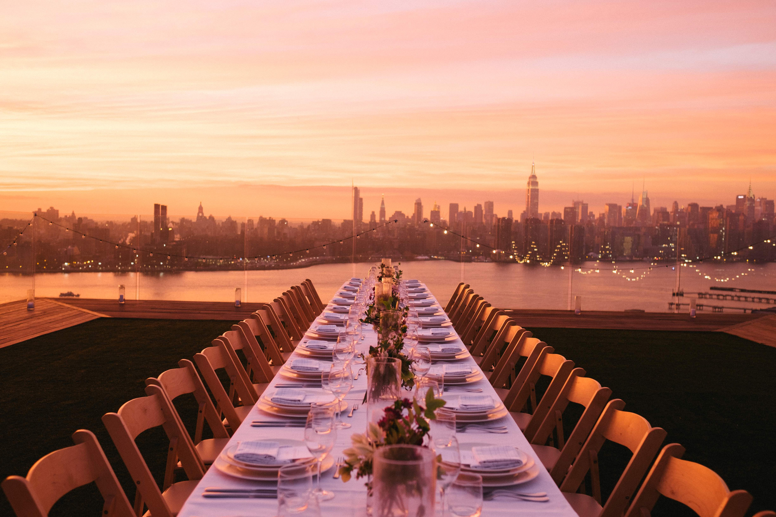 Rooftop dinner table at sunset with city skyline.