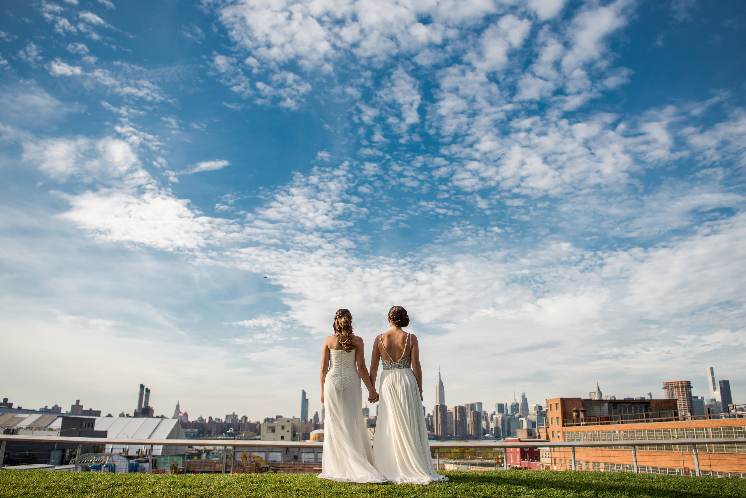 Two brides holding hands facing city skyline. Ask Cha