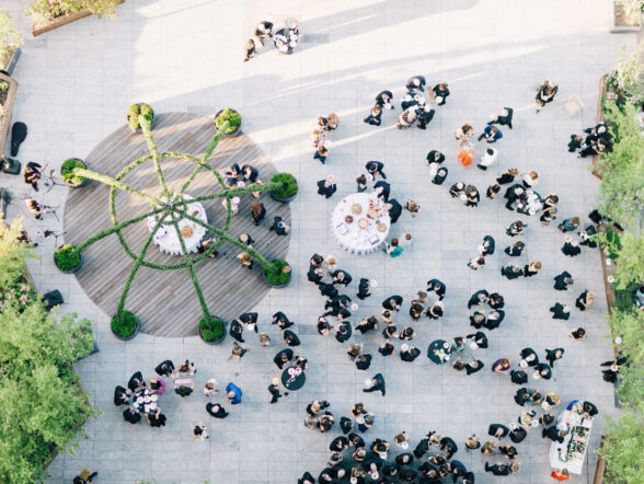 Aerial view of cocktail hour with guests mingling around round tables on a rooftop terrace.