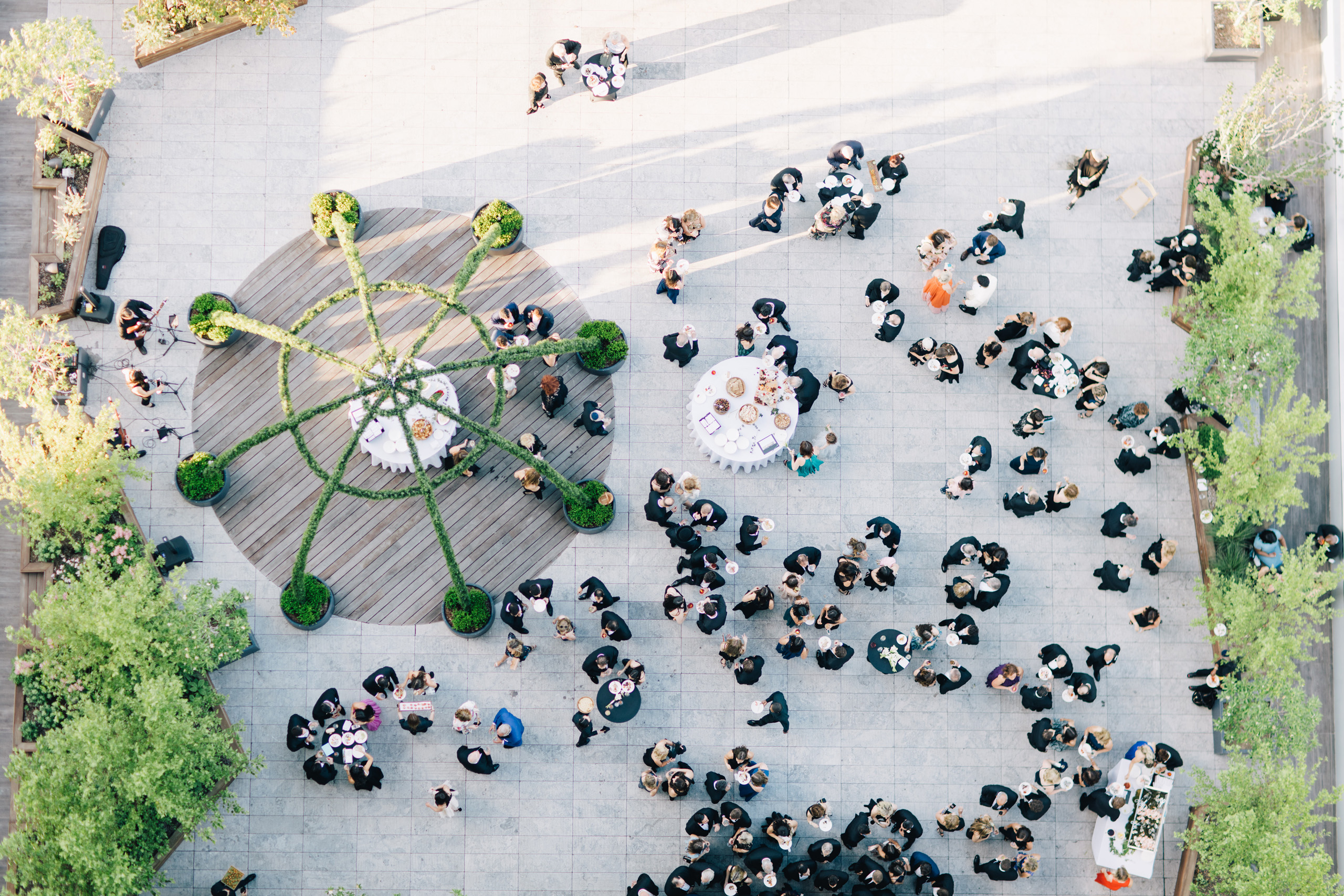 Aerial view of cocktail hour with guests mingling around round tables on a rooftop terrace.