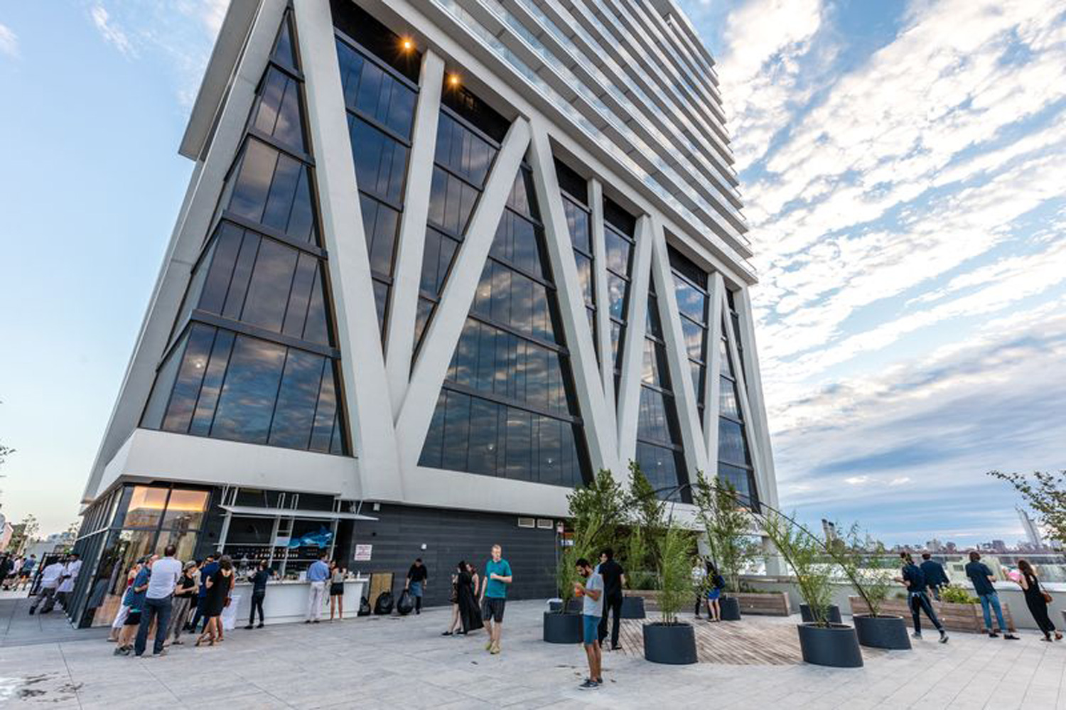 Modern glass high-rise with people gathered on the terrace.